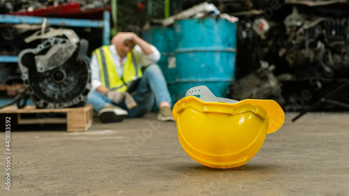 Close up yellow safety hardhat on floor with man stressed and unemployed in factory, standard horizontal banner 16:9.