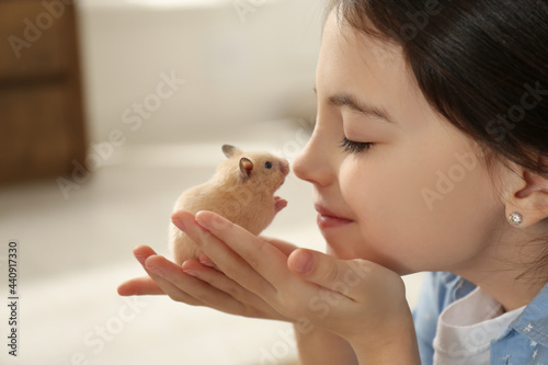 Little girl holding cute hamster at home, closeup