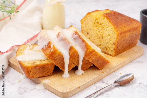 Sliced pound cake topped with lemon glaze on a cutting board and spoon are marble table.