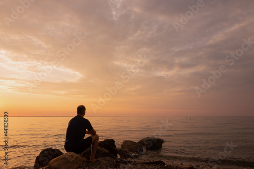 Silhouette of a lonely man sitting on the beach at sunset.