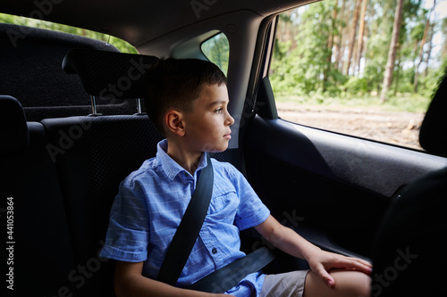 Fastened boy sitting in the safety car booster seat and looking out the window during travel by car