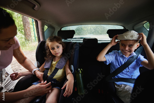 Mother fastening her daughter to child safety seat inside car. Children on safety booster car seat inside the vehicle