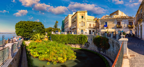 The Fountain of Arethusa and Siracusa (Syracuse) in a sunny summer day. Sicily, Italy. The Fountain of Arethusa in Ortygia, historical centre of Syracuse, Sicily, Italy.