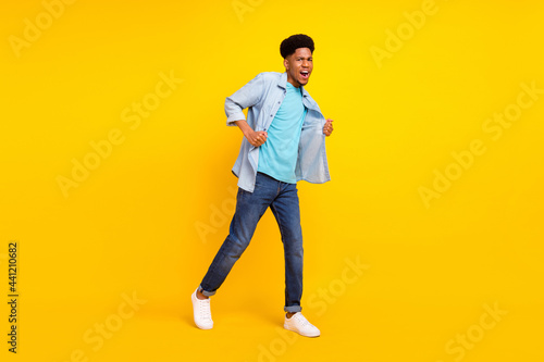 Photo of funny cool dark skin guy dressed denim shirt walking dancing singing isolated yellow color background