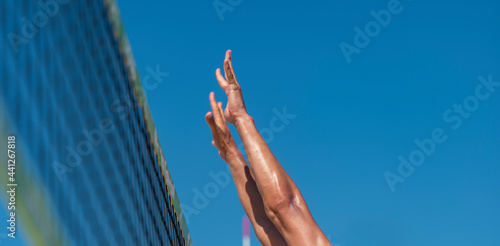 Athletic man jumping to make wall block at beach volleyball net