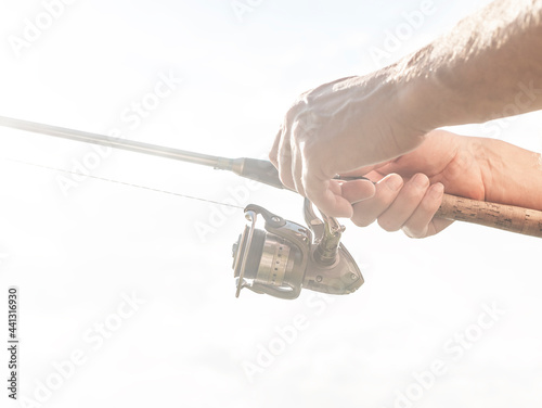 Fisherman hands close up holding spinning reel rod or spoon bait over white overexposed foggy dreamy background.