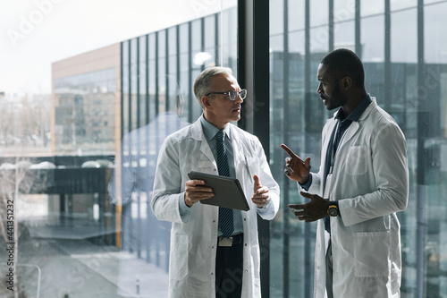 Waist up portrait of two doctors talking while standing by window in conference room, copy space