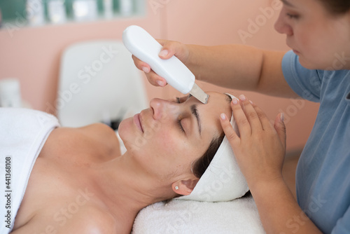 Ultrasonic skin cleaning procedure of face. Skin Care. Close-up of beautiful woman receiving ultrasound facial peeling. Beauty treatment and cosmetology in spa salon.