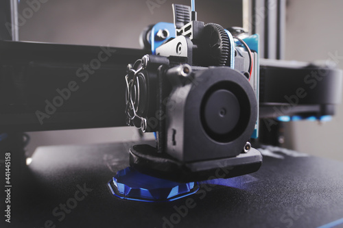 black FDM 3D printer manufactures a hollow part from metallic blue plastic in thick layers - additive manufacturing concept with selective focus