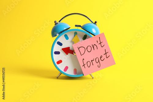 Alarm clock and reminder note with phrase Don't forget on yellow background