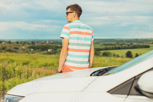Young male enjoying the beautiful landscape while driving his car, a man standing near his car