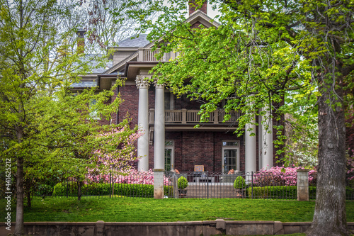 Side of historical old home with ornate pillars and balconies in springtime with pink flowering trees and bushes