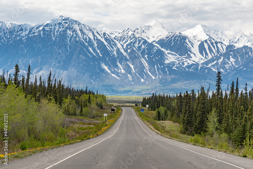 Alaska Highway driving into Haines Junction town in spring time with epic, huge mountains in far distance with amazing scenic drive ahead. Tourists, tourism shot for camping, RV, road trip. 