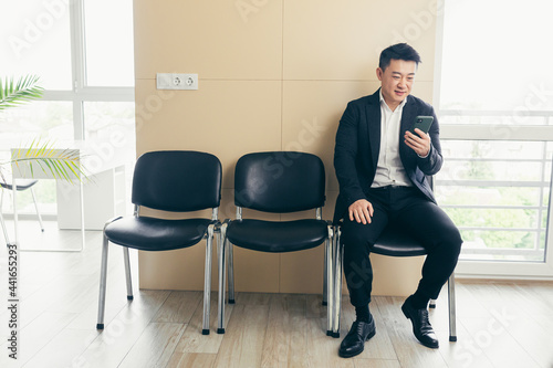 Male asian businessman got good news, rejoices in the waiting room for an interview, near the reception of a modern business center