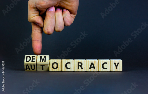 Democracy or autocracy symbol. Businessman turns wooden cubes and changes the word autocracy to democracy. Beautiful grey background, copy space. Business and democracy or autocracy concept.