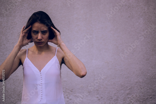 wful headache. Woman having headache with her head in her hands on gray wall background. looking at the camera