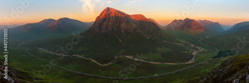 Panorama of Glencoe mountain range covered in beautiful golden light from the evening sun. Majestic landscape of the Scottish Highlands, UK.