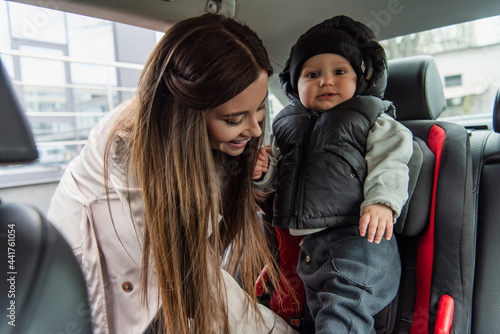 smiling woman putting little son into baby car chair
