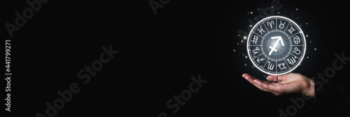 Women's hand in the dark holding glowing astrological signs of the zodiac in a circle. Banner
