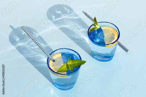 summer drink. cool refreshing beverage with mint and lemon in colored glass with paper tube. zero waste home. minimalism. natural fresh lemonade with hard shadows on blue background