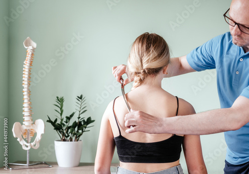 Osteopath practitioner performing fascia release maniupulations using IASTM treatment, girl receiving soft tissue treatment on her neck with stainless steel tool