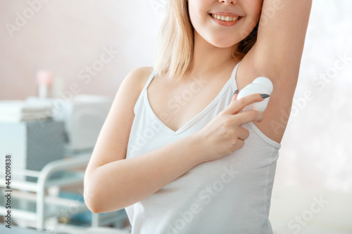 Hygienic deodorant applying in female hands. Young woman use antiperspirant in armpit after shower in bathroom. Morning routine in front of mirror. Self Care hygiene.