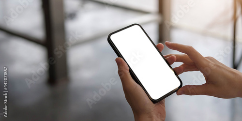 Mockup image blank white screen cell phone.women hand holding texting using mobile on desk at home office.