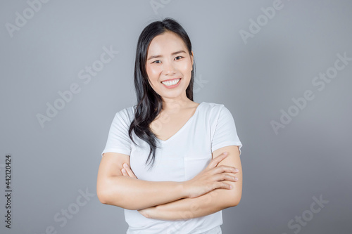 Portrait of smiling Asian woman with long dark hair wears white t-shirt crossed arms isolated on gray background