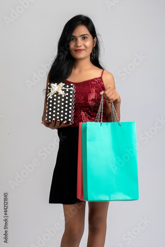Pretty young girl posing with shopping bag and gift box on a grey background