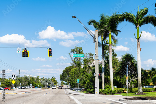 Palm trees on street road in Bonita Springs, Florida with sign for famous Barefoot Beach city town at day in Collier county with blue sky in spring