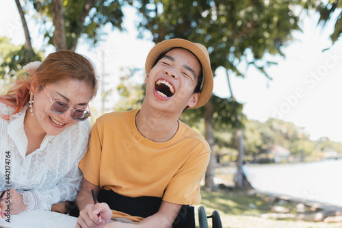 Asian Disabled child and Mother on wheelchair is playing, learning, drawing, reading in the outdoor city park like other people with family, Life in the education age, Happy disability kid concept