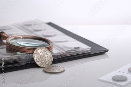 Numismatics. Old collectible coins and a magnifying glass on the table.