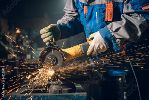 Locksmith in special clothes and goggles works in production. Metal processing with angle grinder. Sparks in metalworking