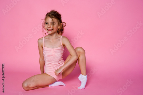 Pretty girl does gymnastics in a leotard on the pink background. children's sports concept.