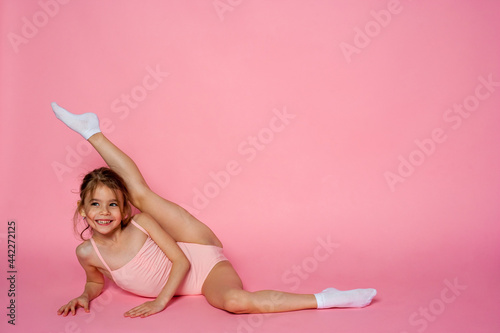 Pretty girl does gymnastics in a leotard on the pink background. children's sports concept.