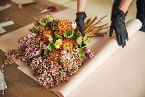 Woman in disposable nitrile gloves wrapping a mixed flower bouquet