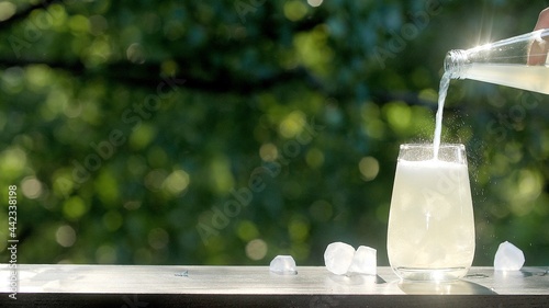 Making drinks outdoors. Hand pours a carbonated drink into a transparent glass with ice. Little splashes fly to the sides from a highly carbonated drink. Many ice cubes in a glass and around
