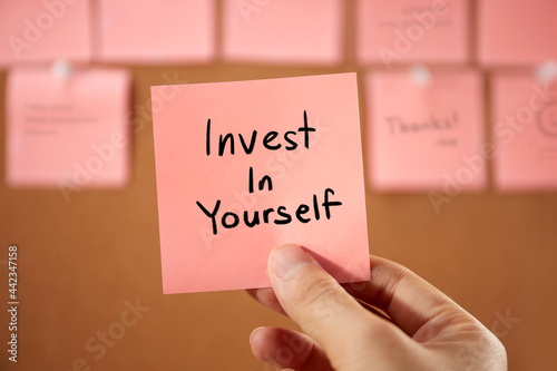 Hand holding a sticky note text sign showing Invest In Yourself