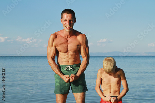 Father and son having fun on the beach and showing muscles . Being a good example to your child concept