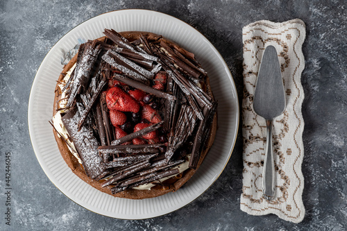 Top view of chocolate marquise cake with red berries resting on a rustic table.