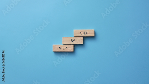 Wooden cubes in the form of a ladder and an inscription: step by step. Symbolic image of the movement to the goal