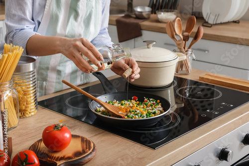 Woman cooking tasty rice with vegetables on stove in kitchen, closeup