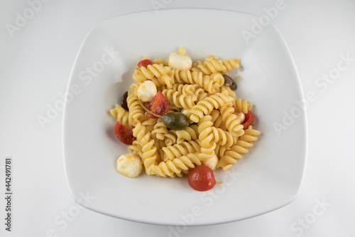 Piatto di pasta con pomodori, mozzarella, olive e capperi su sfondo bianco