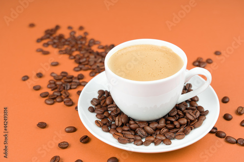 A cup of creamy coffee with roasted coffee beans, orange color background and copy space