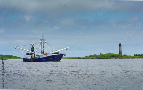 A shrimp boat on the Sabine River heading into the Gulf of Mexico past the historic Sabine Pass lighthouse 