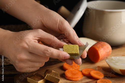 Woman holding bouillon cube at table, closeup