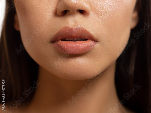 Close-up of woman's lips with fashion natural beige lipstick makeup. Macro sexy pale lipgloss make-up . Gentle pure skin and wavy brunet hair. Cosmetology, Spa, increase in lips