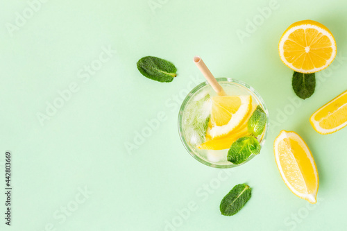 Ice lemon water or lemonade with mint on a green background. A glass of fresh fruit drink for summer heat.