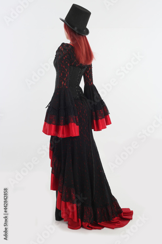 full length portrait of red haired woman wearing long black gothic vampire gown. standing pose on white studio background