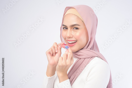 Young muslim woman holding colorful retainer for teeth over white background studio, dental healthcare and Orthodontic concept.